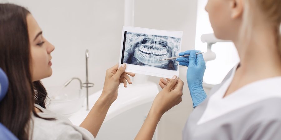 Dentist showing X-ray image to patient. People, medicine, stomatology, technology and health care concept - happy female dentist with teeth x-ray image and patient woman at dental clinic office